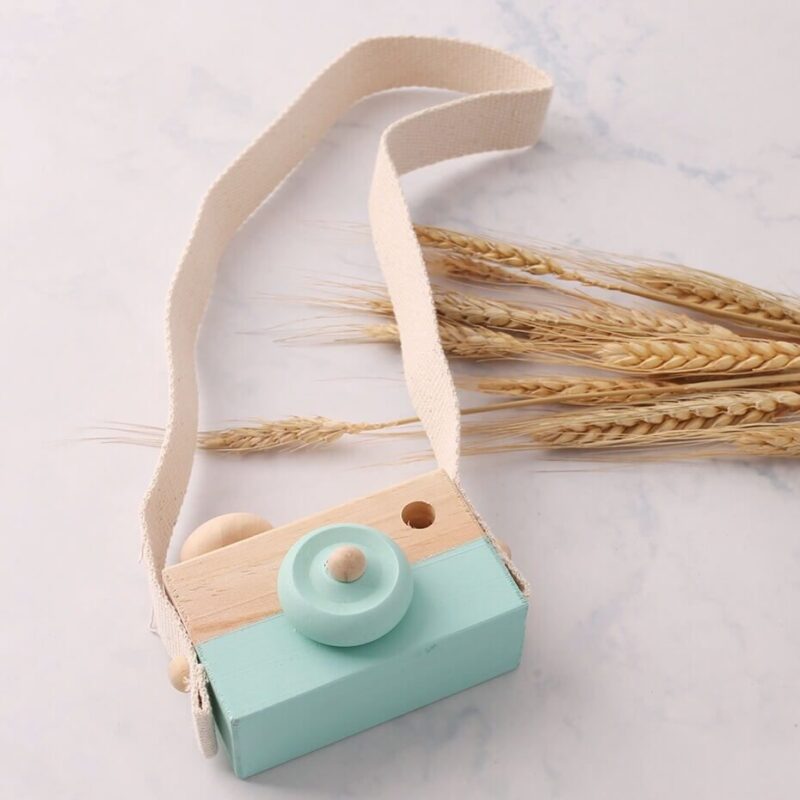 Wooden baby camera green over a marble background and 9 wheat ears placed decoratively to the right.