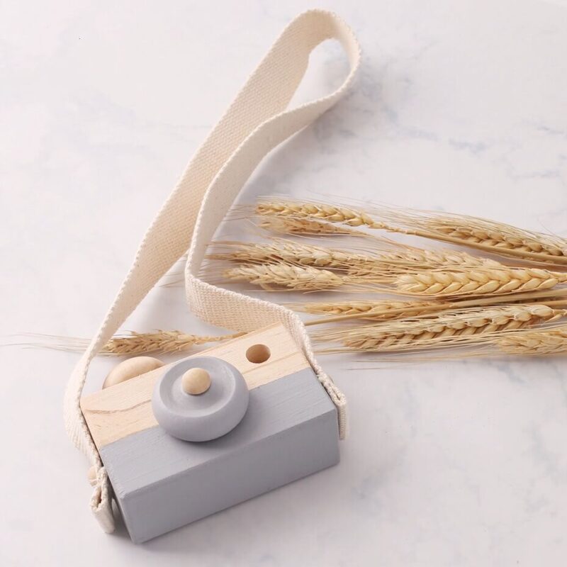 Wooden baby camera grey over a marble background and 9 wheat ears placed decoratively to the right.