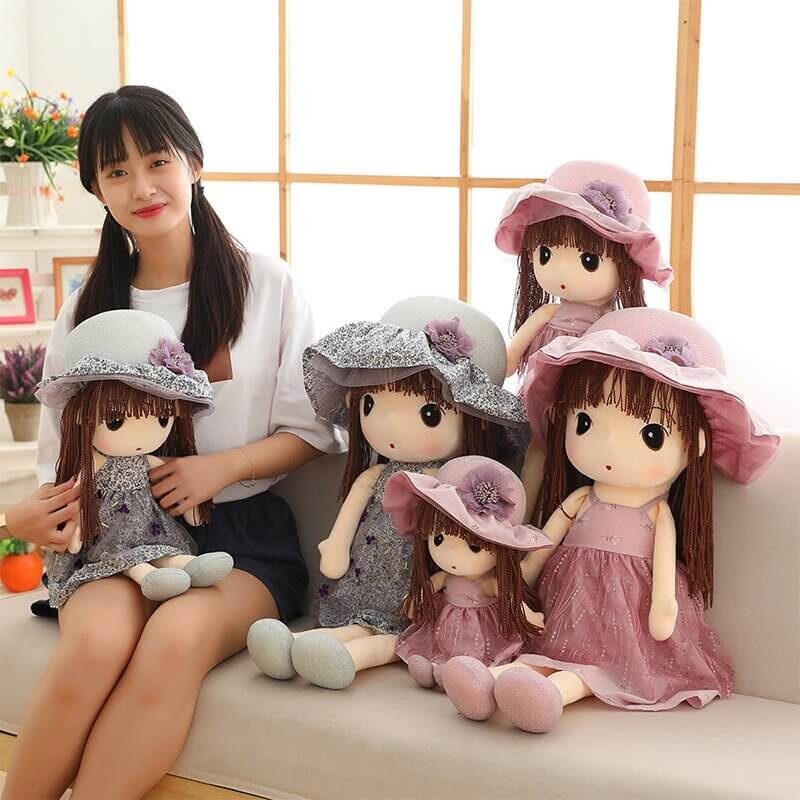 Five blue and pink race day sun hat rag doll friends sat together on the couch with a black haired girl holding one of them in the smallest size to show real life size