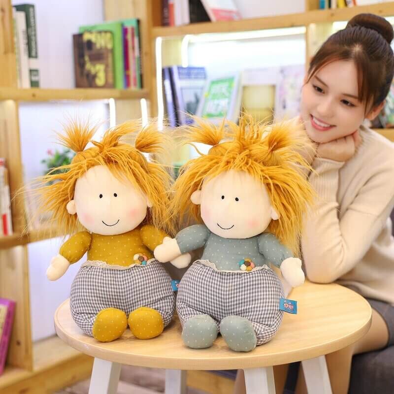 Brown haired girl looking admirably and smiling at yellow and blue playful dolls set up on a table from behind.